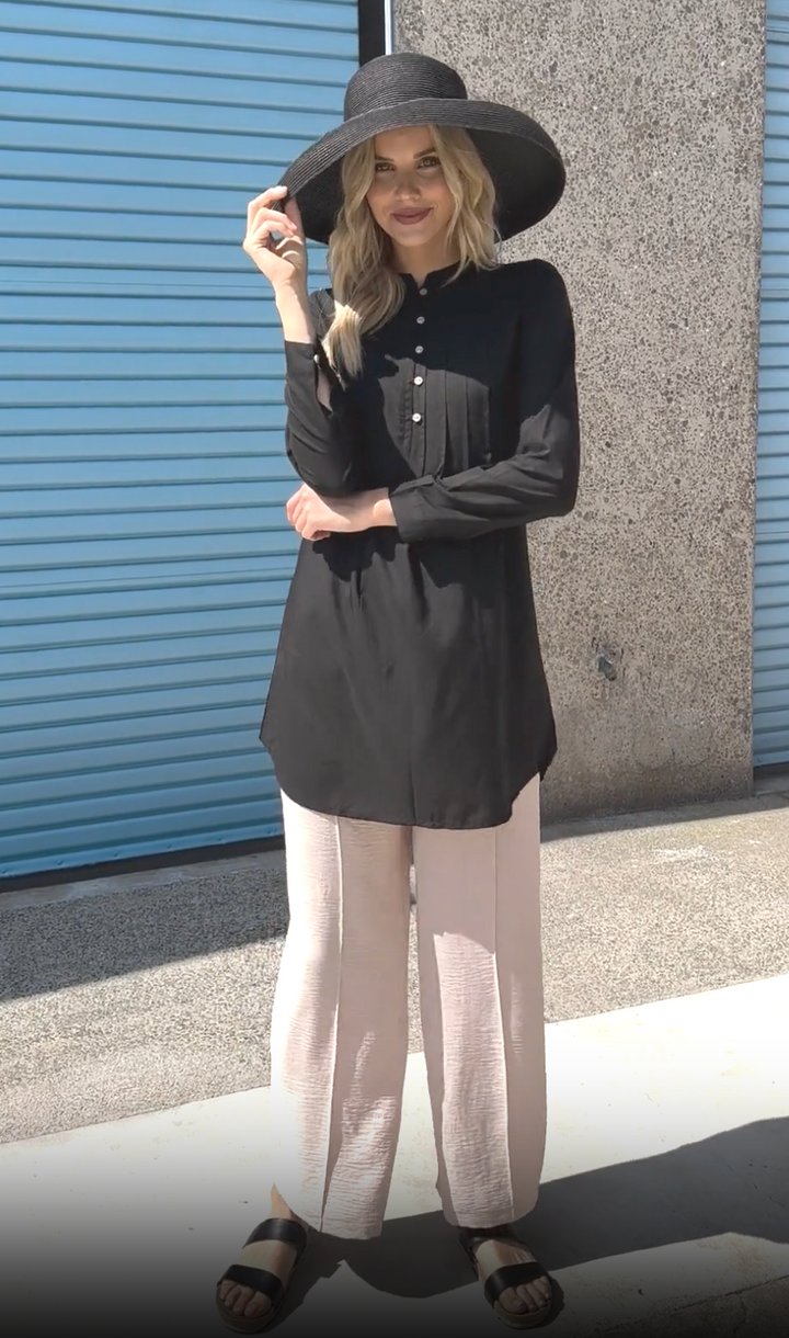 Woman outside wearing black hate with Hurin tunic in Black with Tina Pants in Cream and black sandals. 