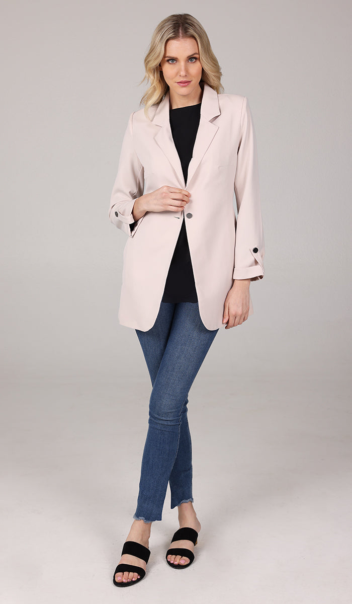 woman wearing a cream blazer jacket with black top inside and blue jeans..