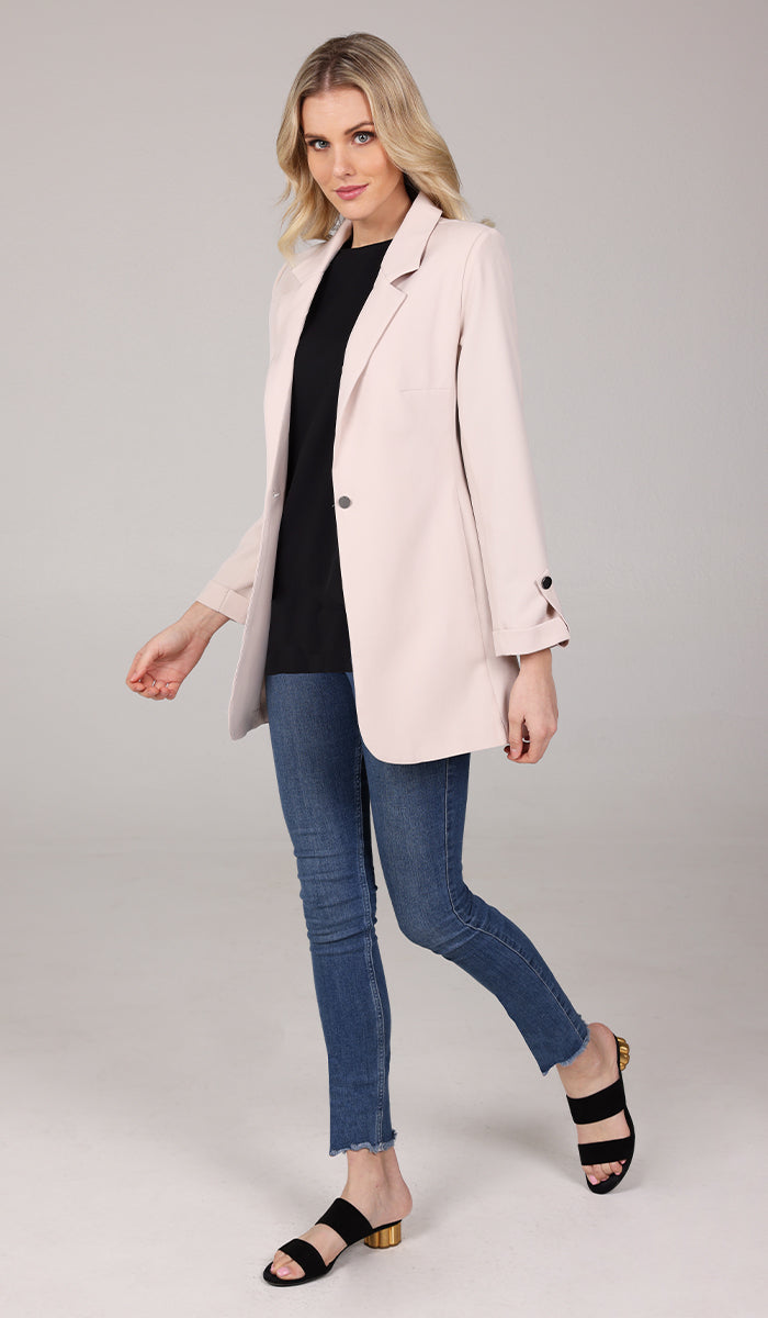 side view of woman wearing a cream blazer jacket with black top inside and blue jeans.