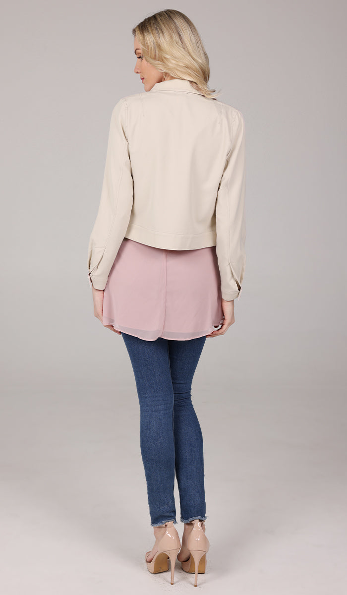 back view of a woman wearing a cream cropped jacket with a blush top and blue jeans.