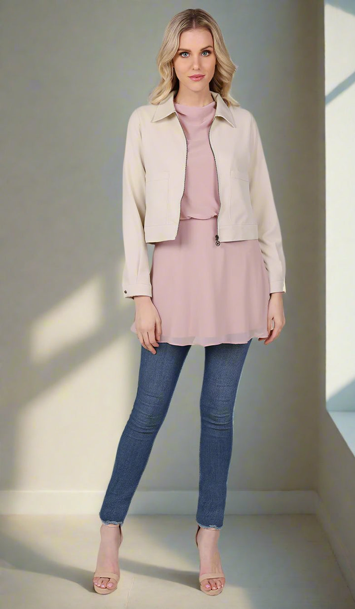 front view of a woman wearing a cream cropped jacket with a blush top and blue jeans.