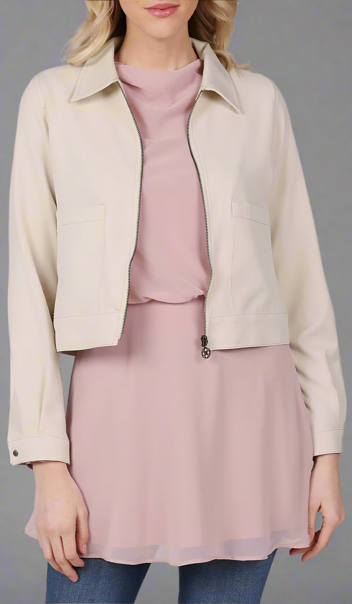 up close view of a woman wearing a cream cropped jacket with a blush top.