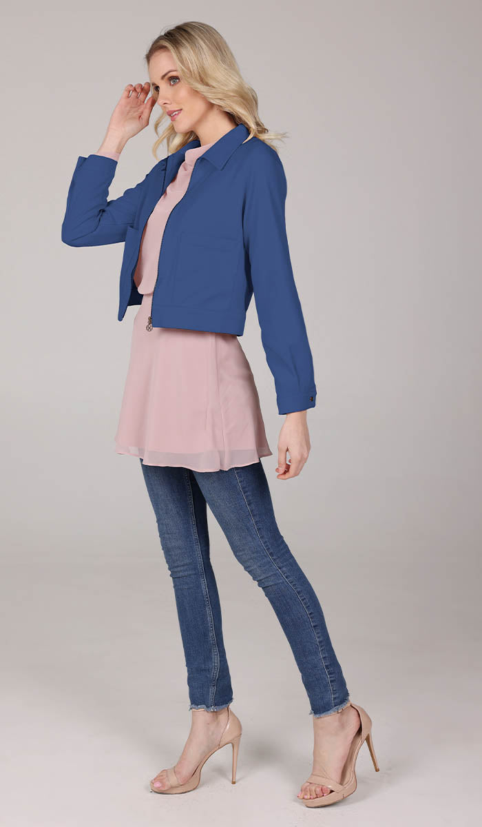 side full body view of a woman wearing a blue cropped jacket with a blush top and blue jeans.