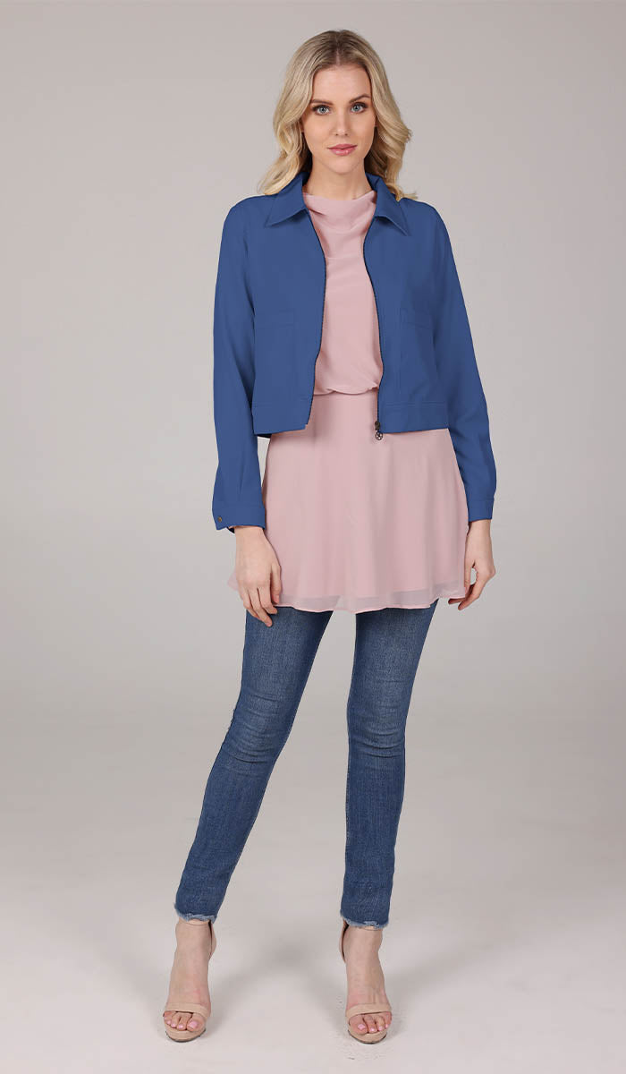 full body view of a woman wearing a blue cropped jacket with a blush top and blue jeans.