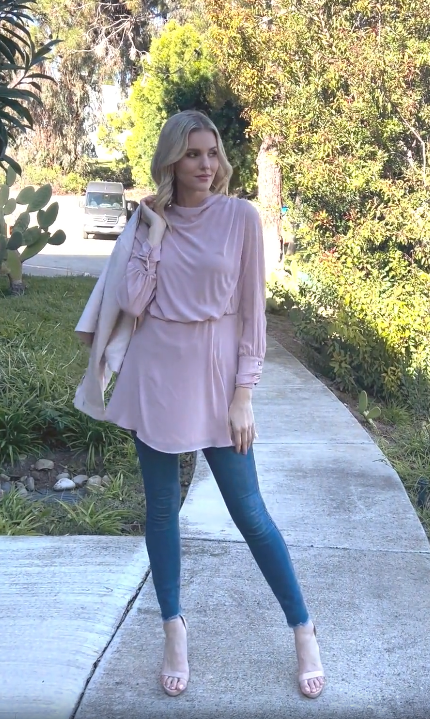 Woman surrounded by greenery wearing Myra modest tunic in Tearose with jeans and heels. 