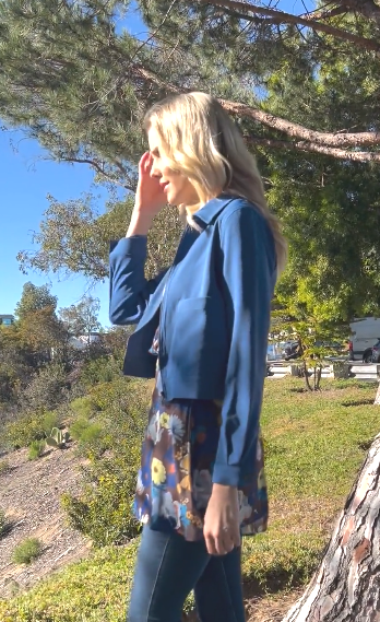 woman looking at the sun wearing a blue cropped jacket with a floral top at a park. 