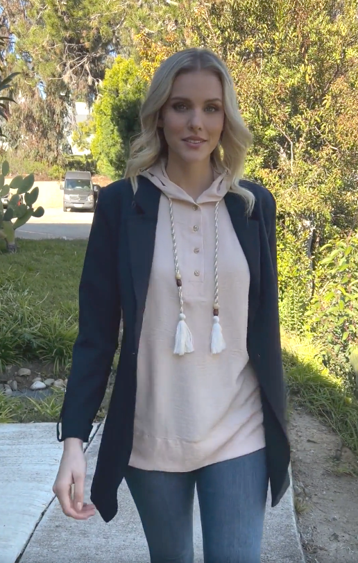 woman wearing a cream hoodie inside a navy blue blazer at a park.