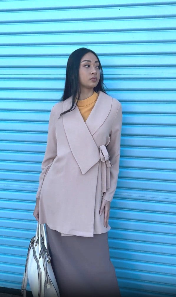 Woman standing in front of blue wall wearing Abeer jacket in Cafe. 