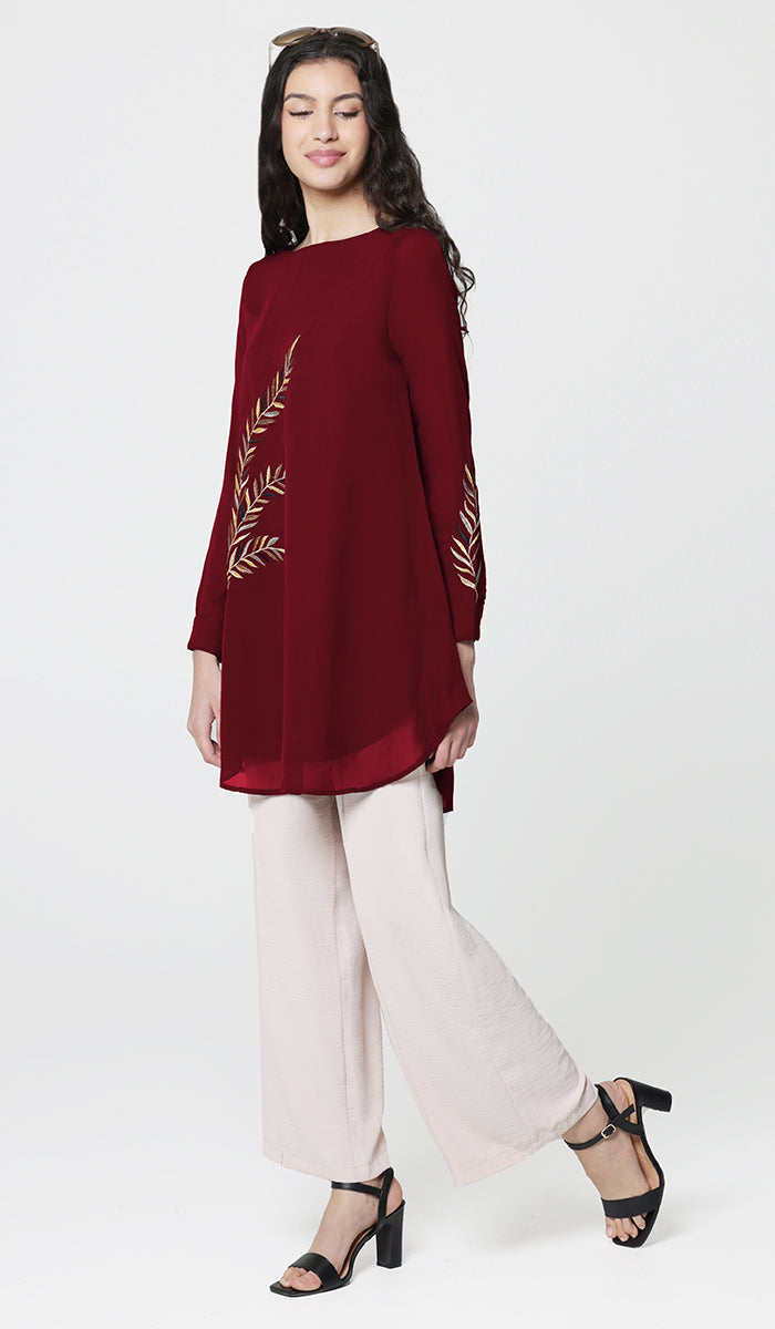 Side view of woman wearing Baraka tunic in Ruby with white pants and heels. 