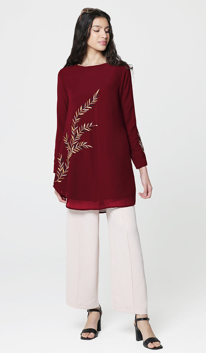 Woman wearing Baraka tunic in Ruby with white pants and heels. 