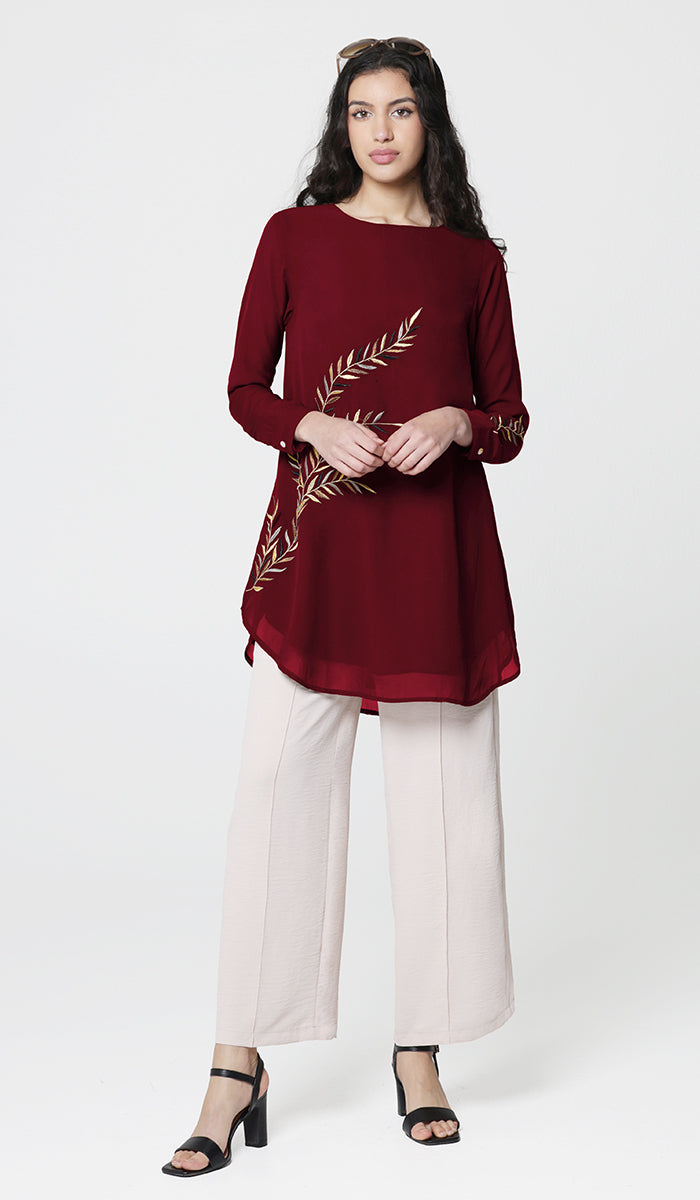 Woman wearing modest Baraka tunic in Ruby with white pants and heels. 