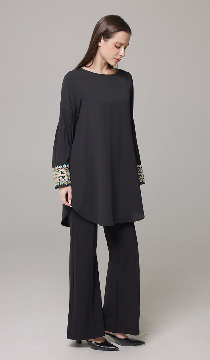 Woman wearing Esme tunic in Black with black pants and heels. 