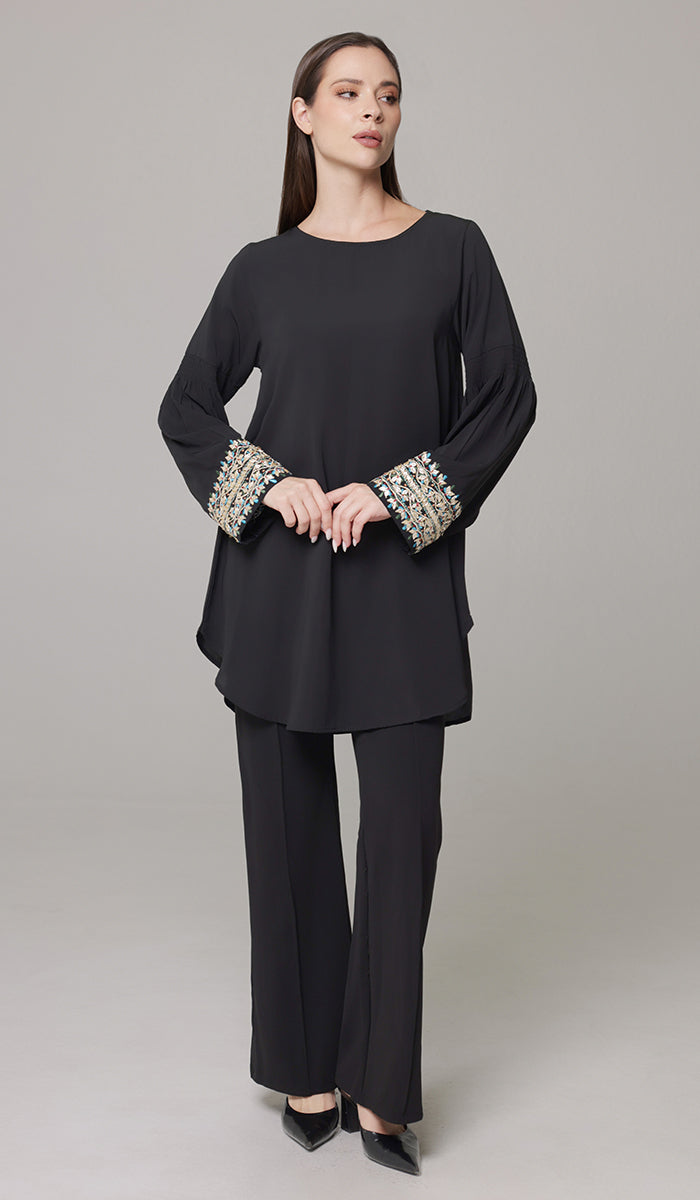 Woman looking to the side wearing embroidered Esme tunic in Black with black pants and heels. 