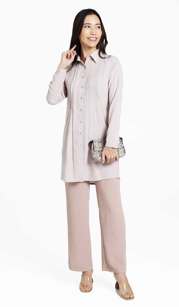 Woman looking to the side wearing Hanane tunic in Blush with khaki pants and heels. 