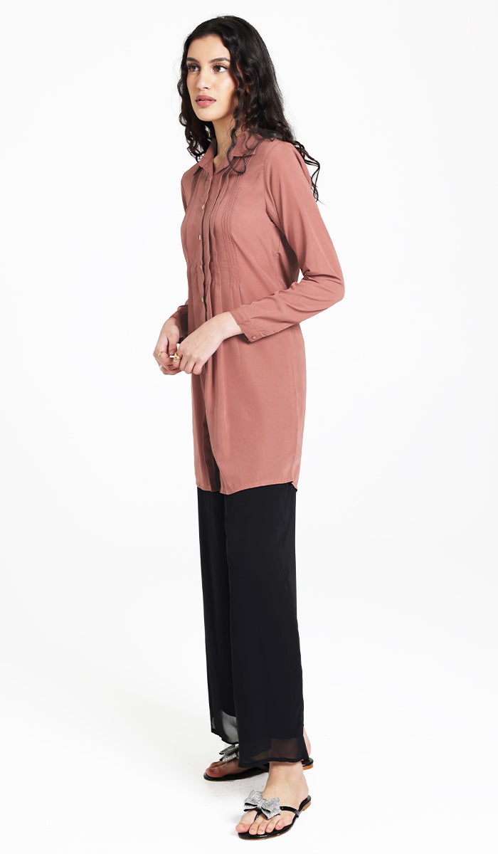 Three-quarter view of woman wearing Hanane tunic in Rose with black pants and sandals. 