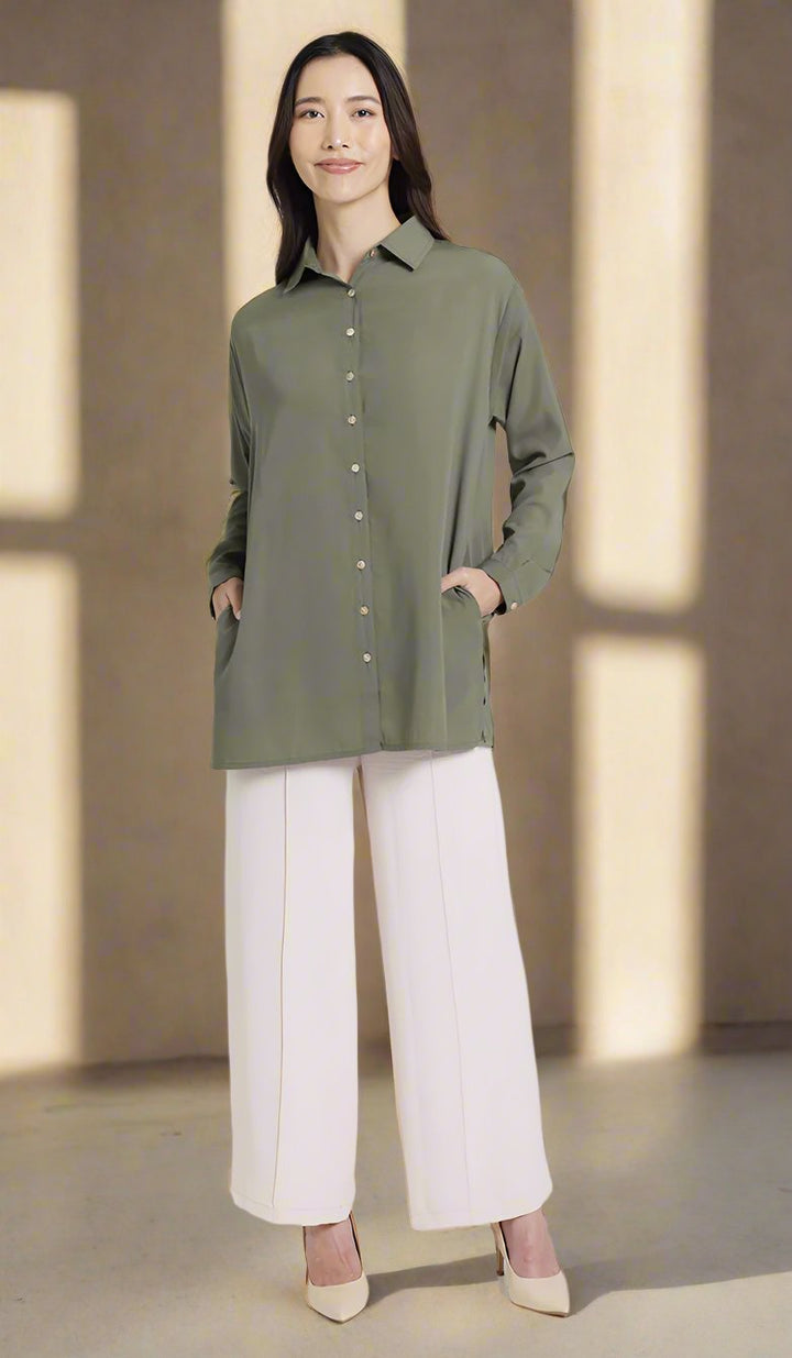 Full front female model wearing an olive boxy button down with side seam pockets.  