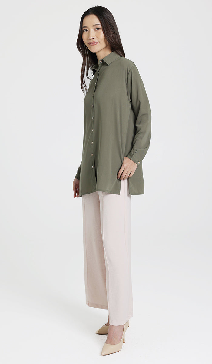 Side view of female model wearing an olive boxy button down with side seam pockets and cream wide leg pants. 