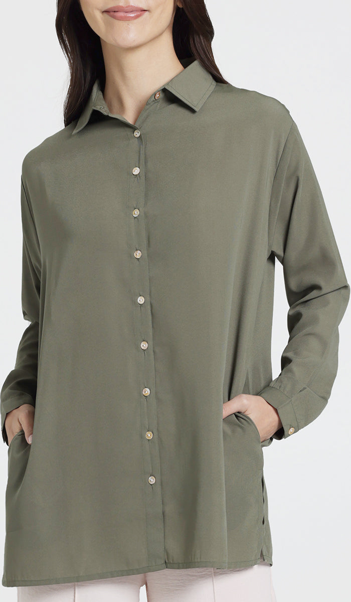 Female model wearing an olive boxy button down with side seam pockets. 