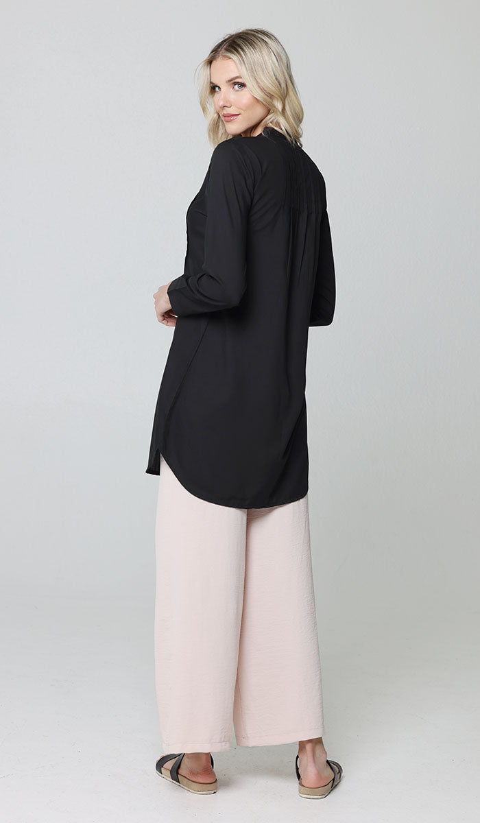 Full body back image of woman wearing modest Hurin tunic in Black with Cream pants and sandals. 