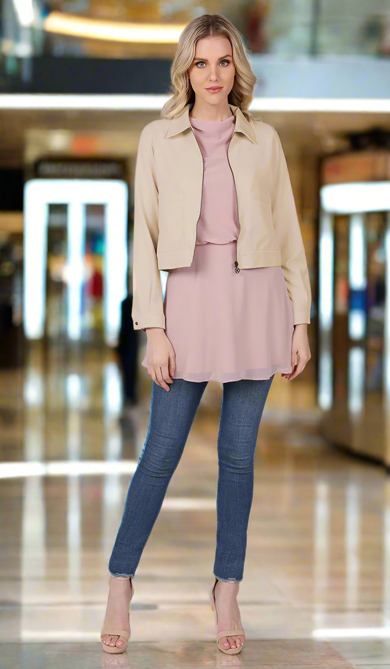 full body view of a woman wearing a tan jacket with blush top and blue jeans.