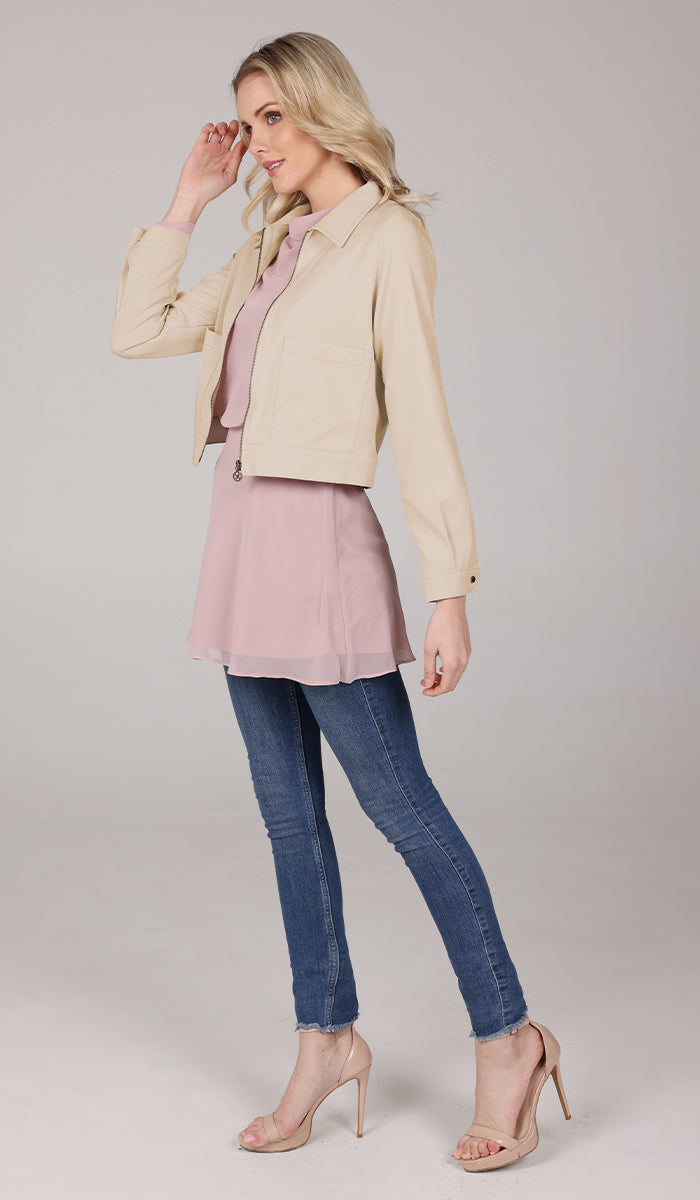 side body view of a woman wearing a tan jacket with blush top and blue jeans.