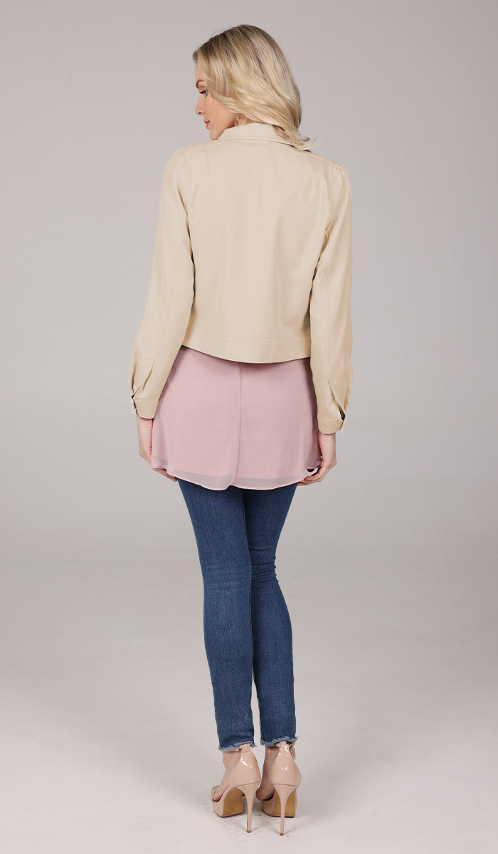 back body view of a woman wearing a tan jacket with blush top and blue jeans.