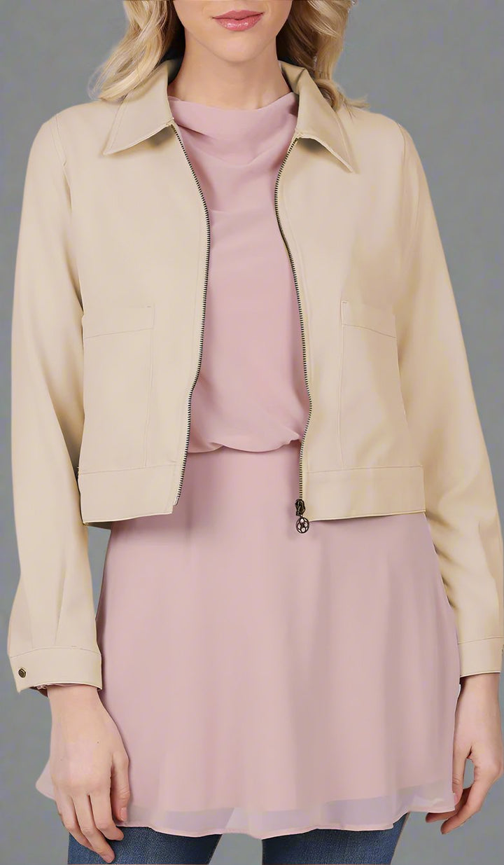 close up view of a woman wearing a tan cropped jacket with a blush top. 