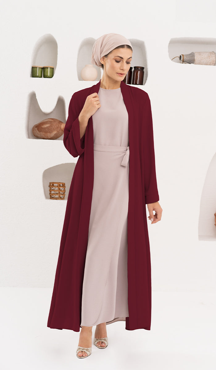 Woman with beige turban wearing a maroon duster jacket  with a decorative background.