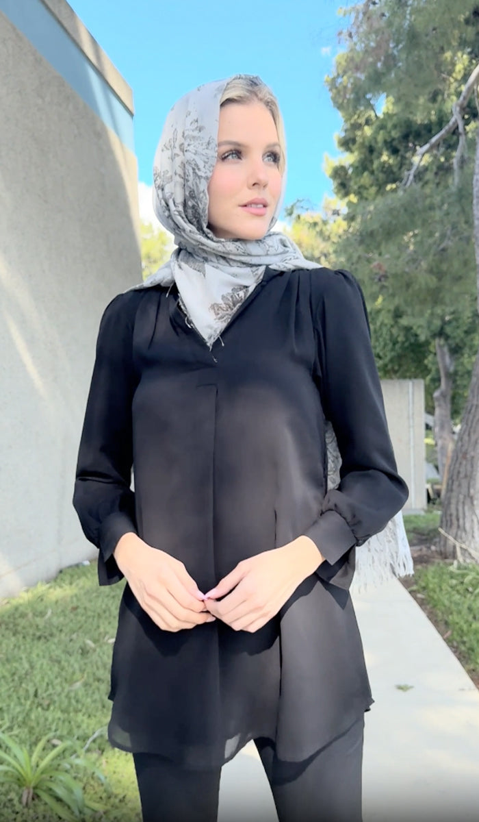 Woman wearing Shaina tunic in Black outside with gray headscarf. 