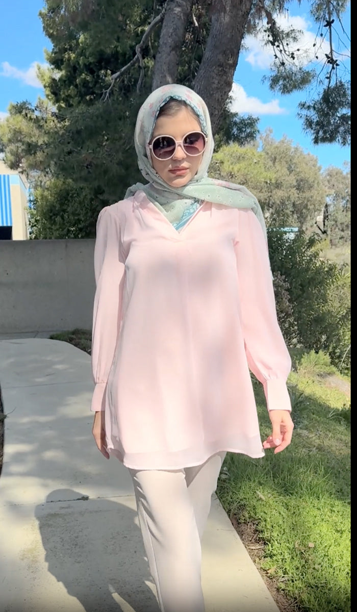 A woman wearing a printed scarf outdoors with a blush Shaina chiffon tunic and cream pants. 