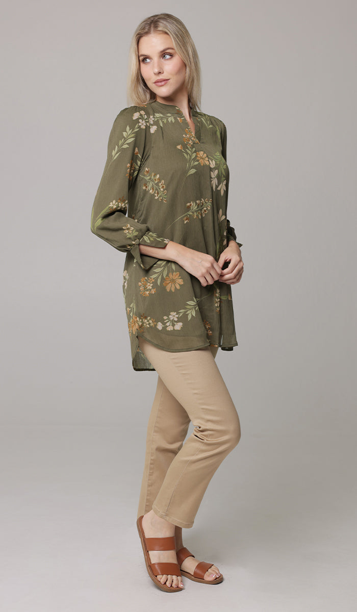 Woman looking over her shoulder wearing Shaina tunic in Olive with khaki pants and sandals. 