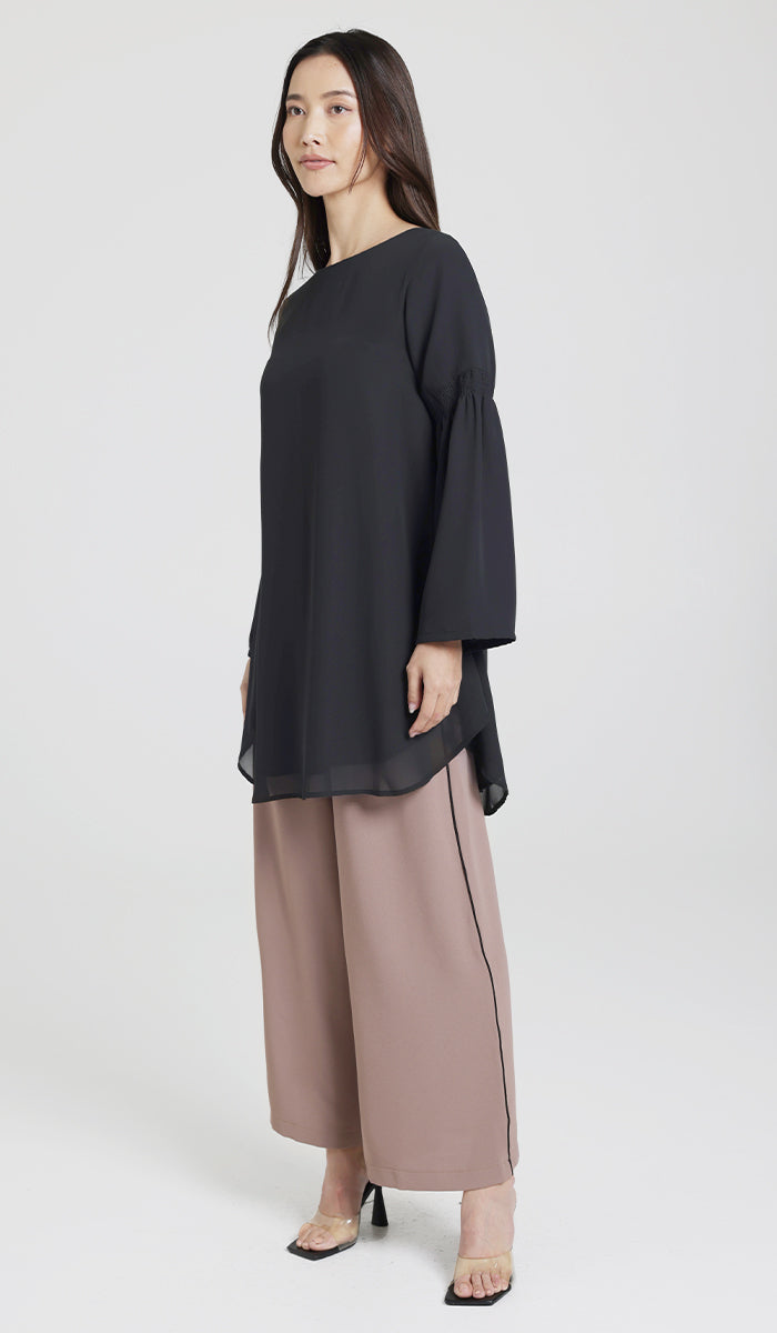 Model posed wearing black modest tunic, brown and black pants, and clear and black heels. 