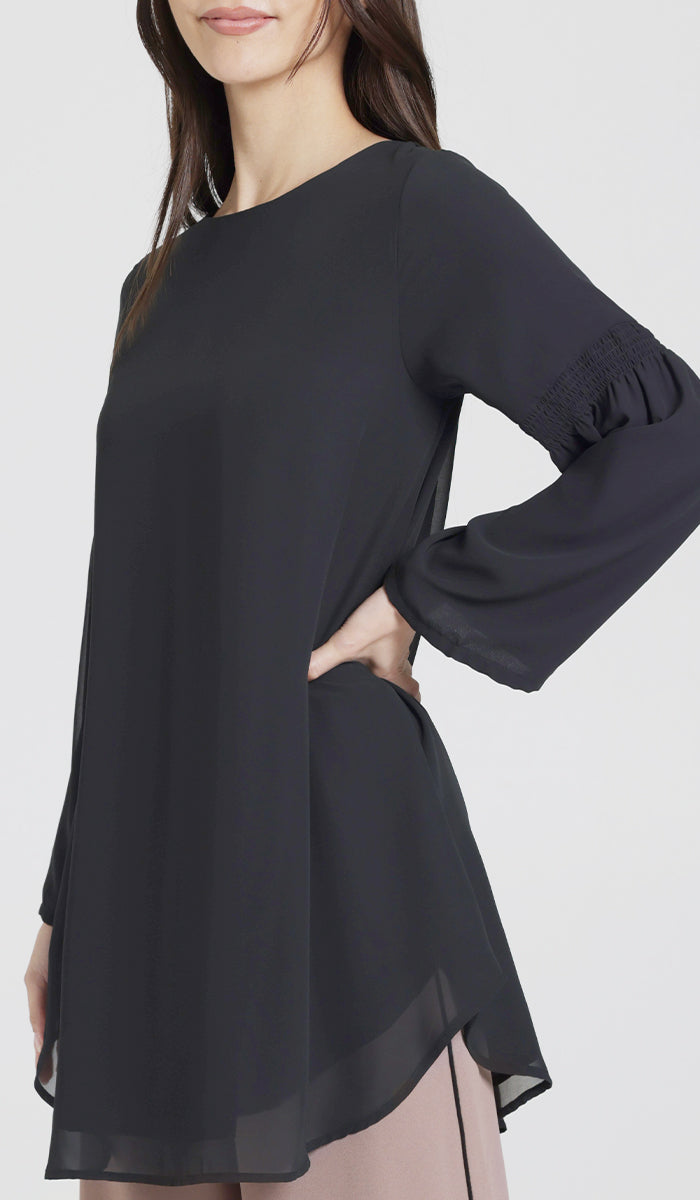 Model wearing modest black tunic, with her arm at her hip. 