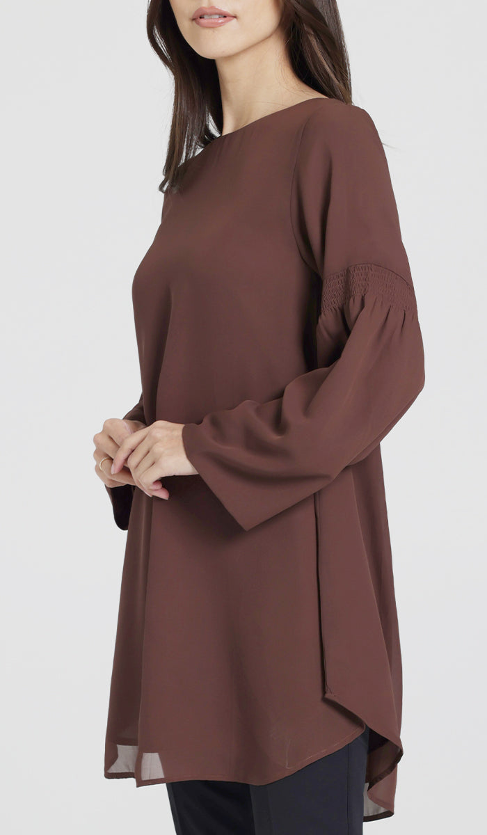 Model posed in modest brown tunic with hands in front of her.