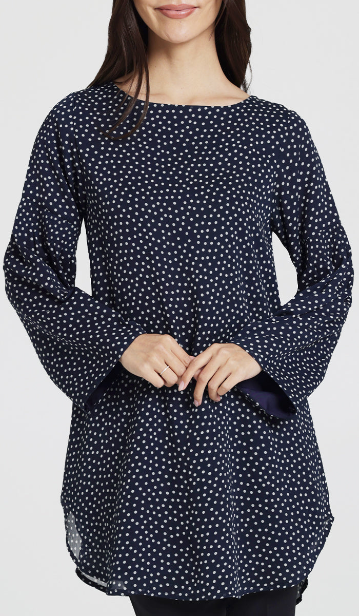 Smiling model wearing navy and white polka dot tunic with hands clasped in front of her. 