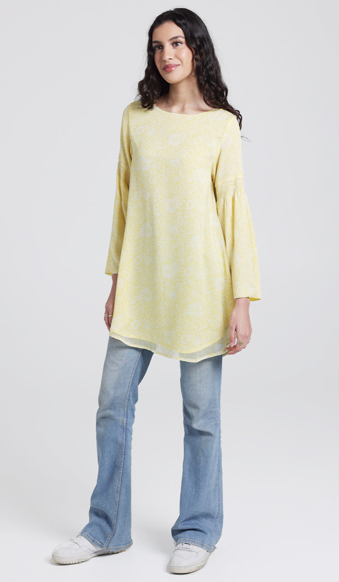 Three-quarter view of model wearing yellow tunic, jeans, and sneakers. 