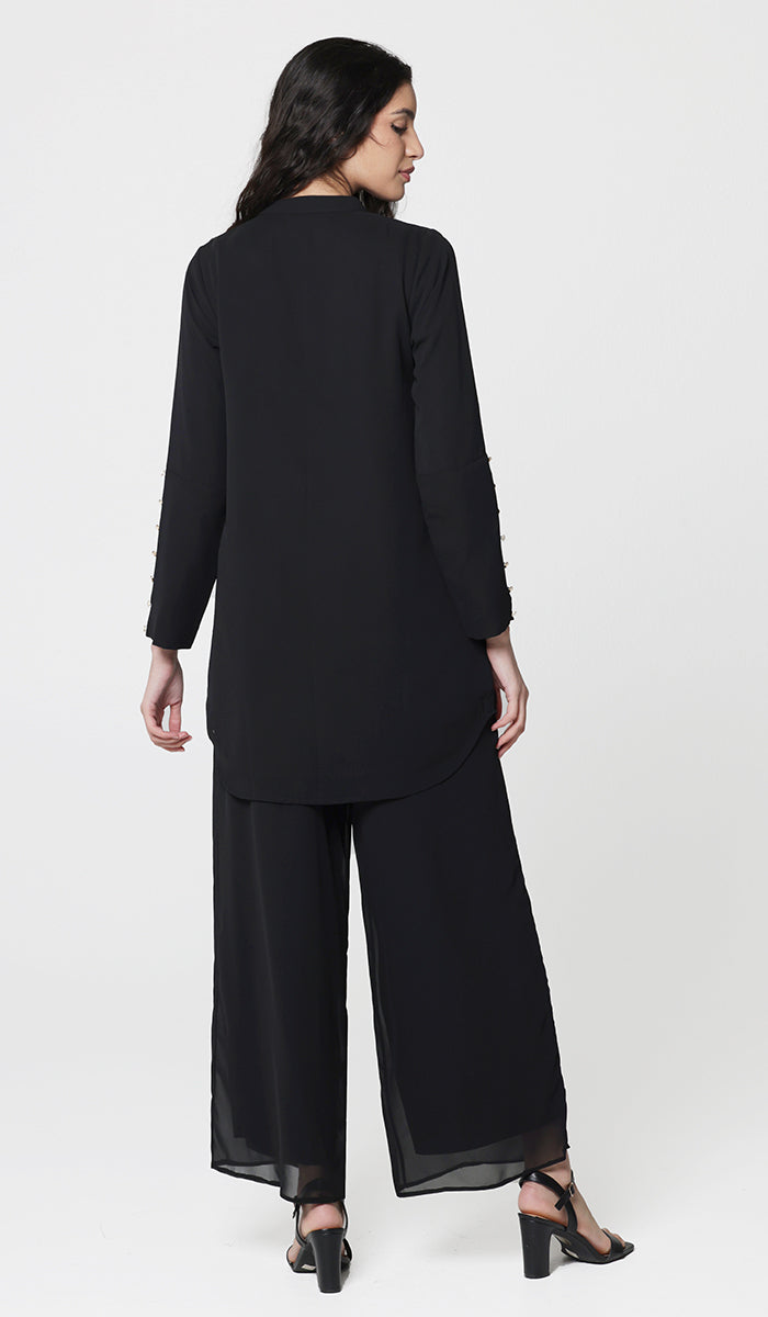 Back view of woman wearing modest Uzma tunic in Black with black pants and heels. 