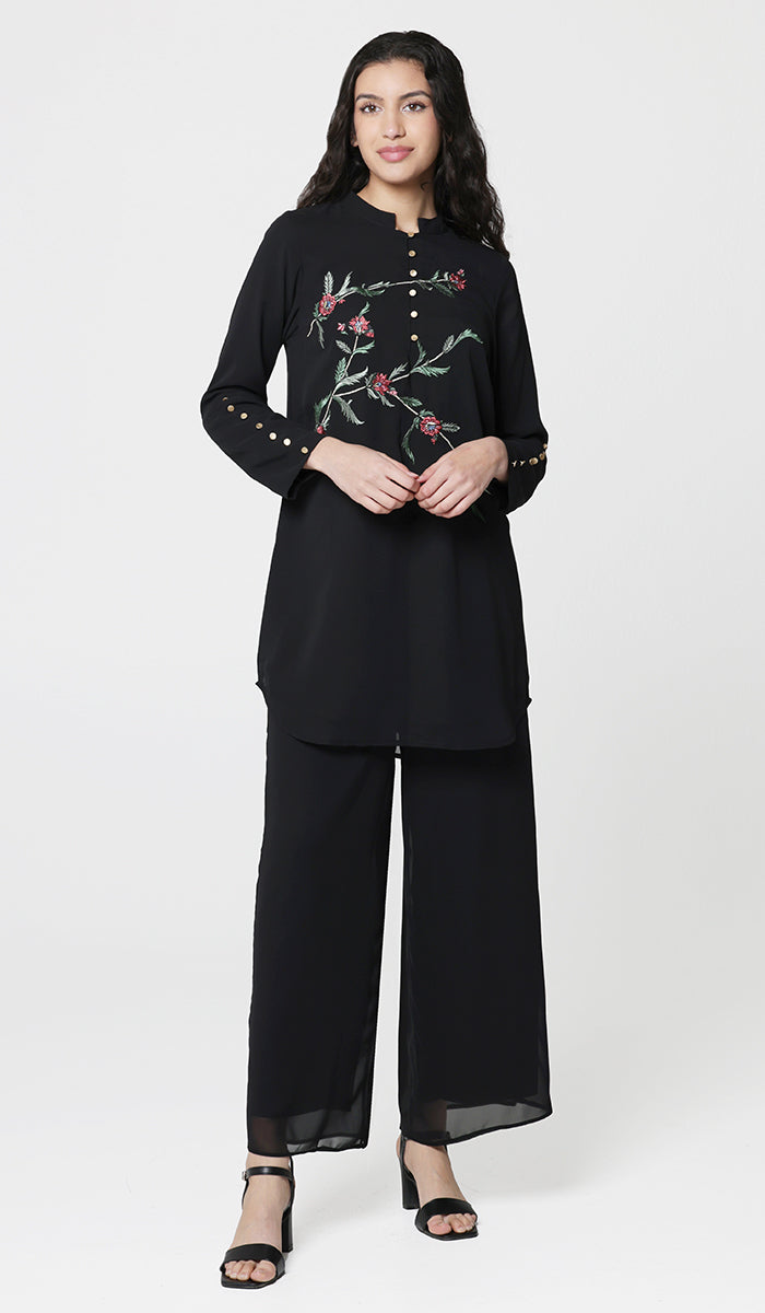 Woman smiling wearing Uzma embroidered tunic in Black with black sandals and pants. 