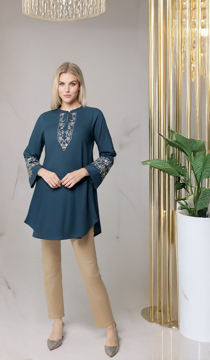 Woman next to plant wearing Zoha tunic in Teal/Gold. 