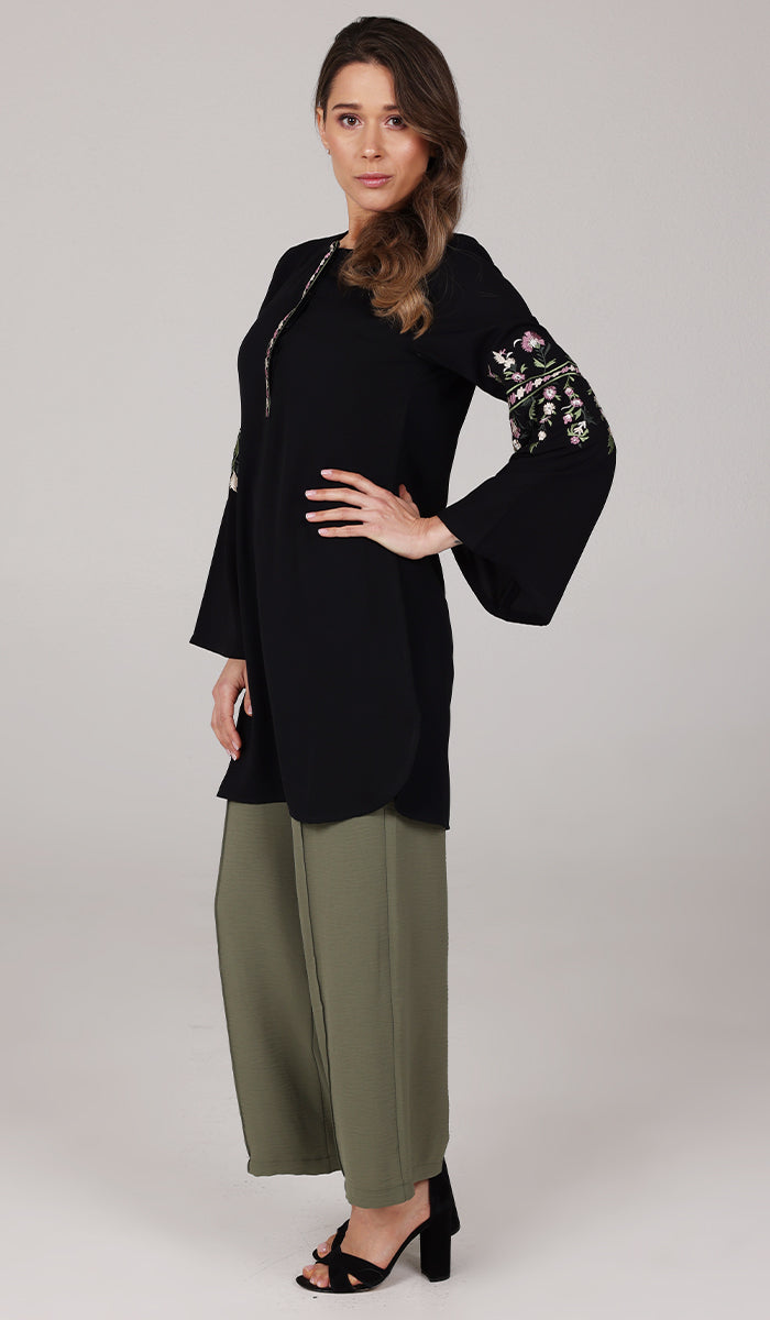 Full body view of model wearing modest Gulzar tunic in Black with green pants and black heels. 