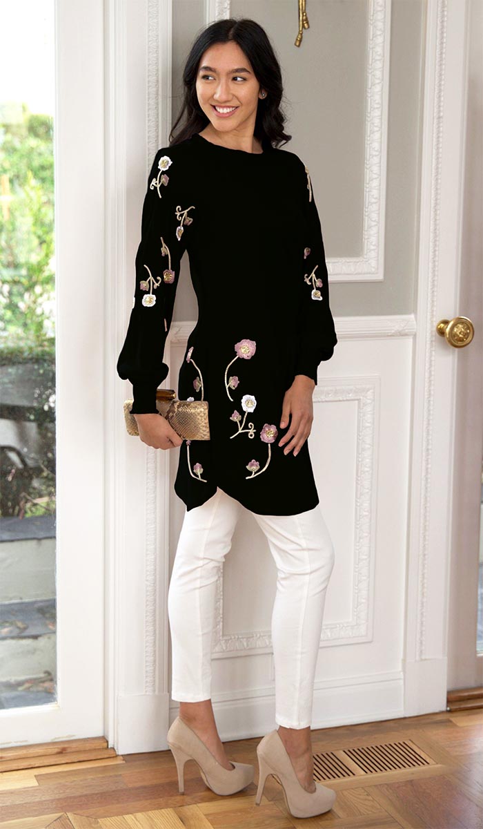 Woman standing in front of door wearing Iman tunic in Black with white pants and heels. 