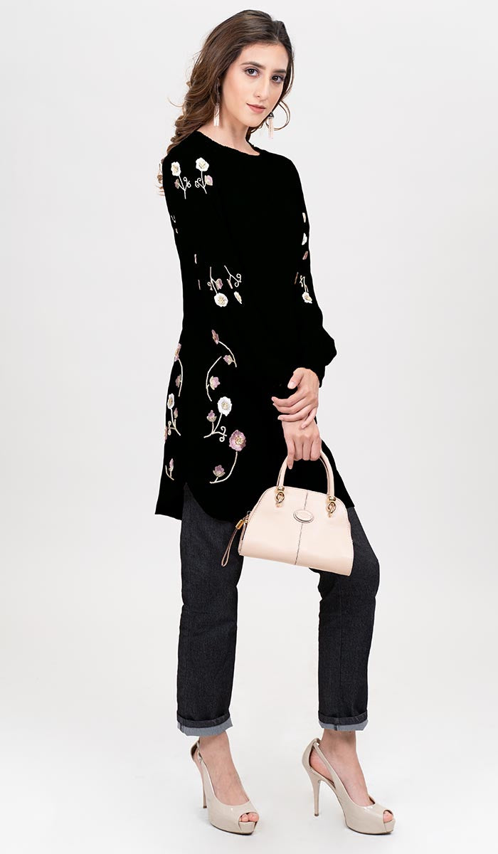 Side view of woman wearing Iman tunic in Black with jeans, heels, and a handbag. 