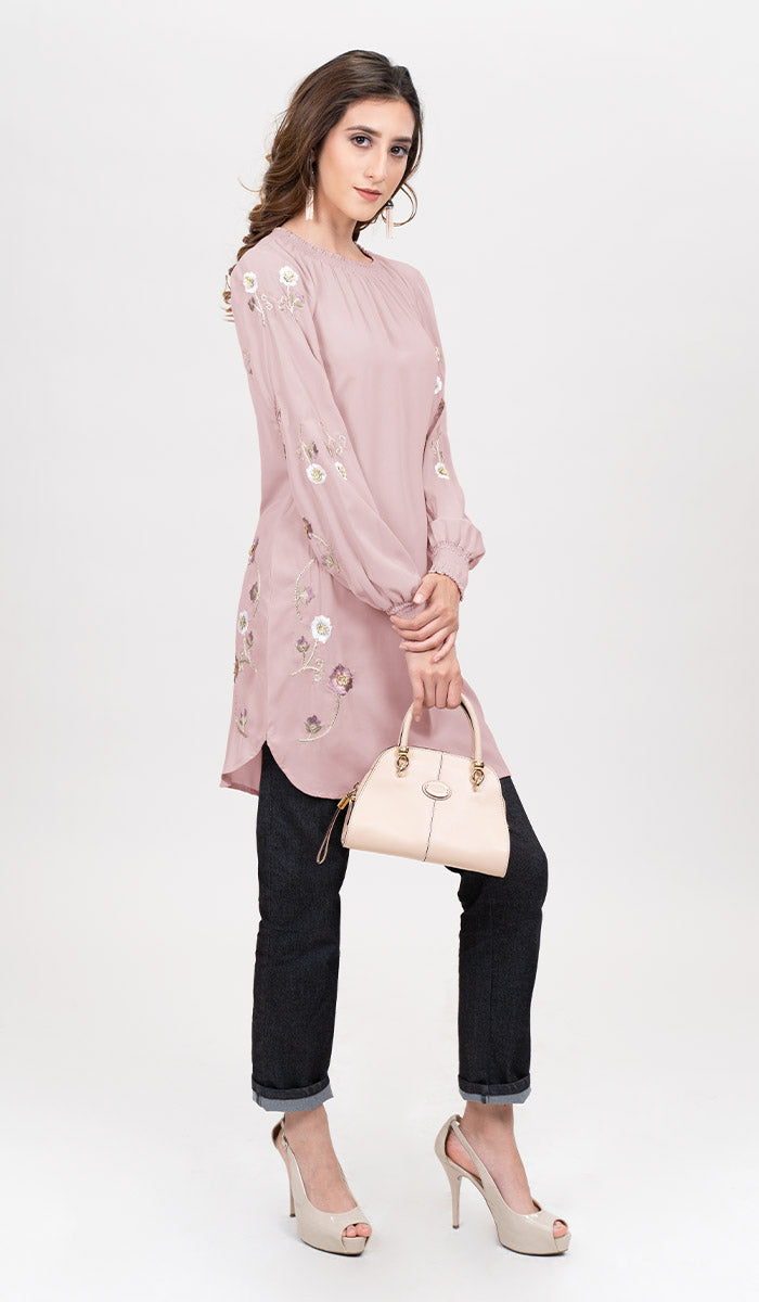 Side view of woman wearing Iman tunic in Blush Pink with jeans, heels, and a handbag. 