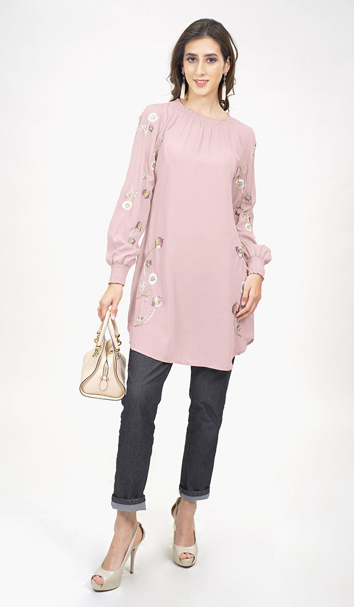 Woman wearing modest Iman tunic in Blush Pink with jeans, heels, and a handbag. 