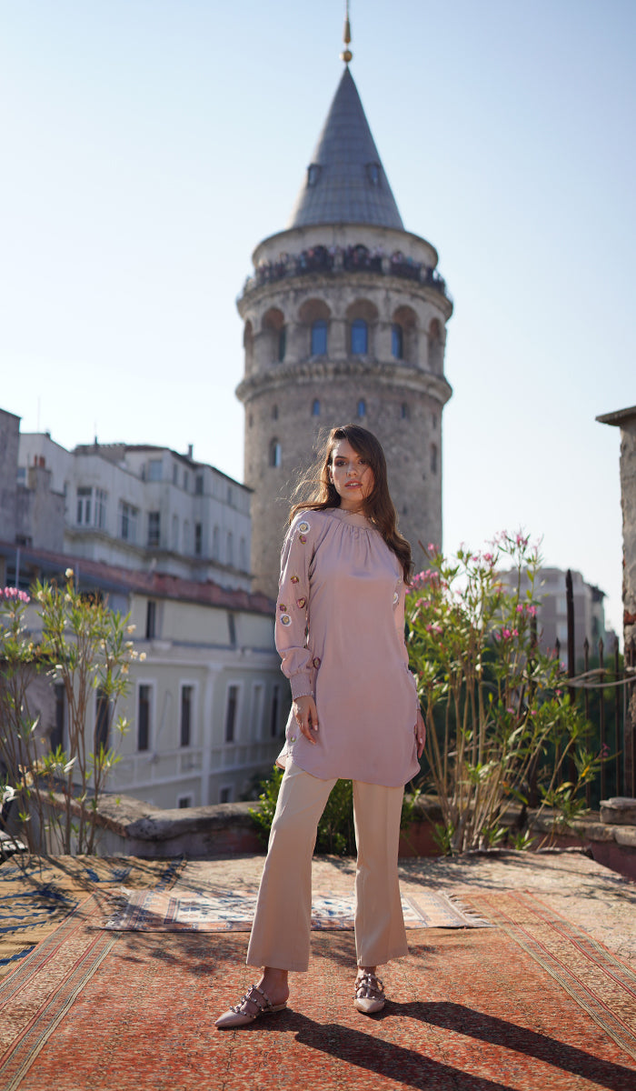 Woman standing in front of building wearing Iman tunic in Blush Pink, khaki pants and flats. 