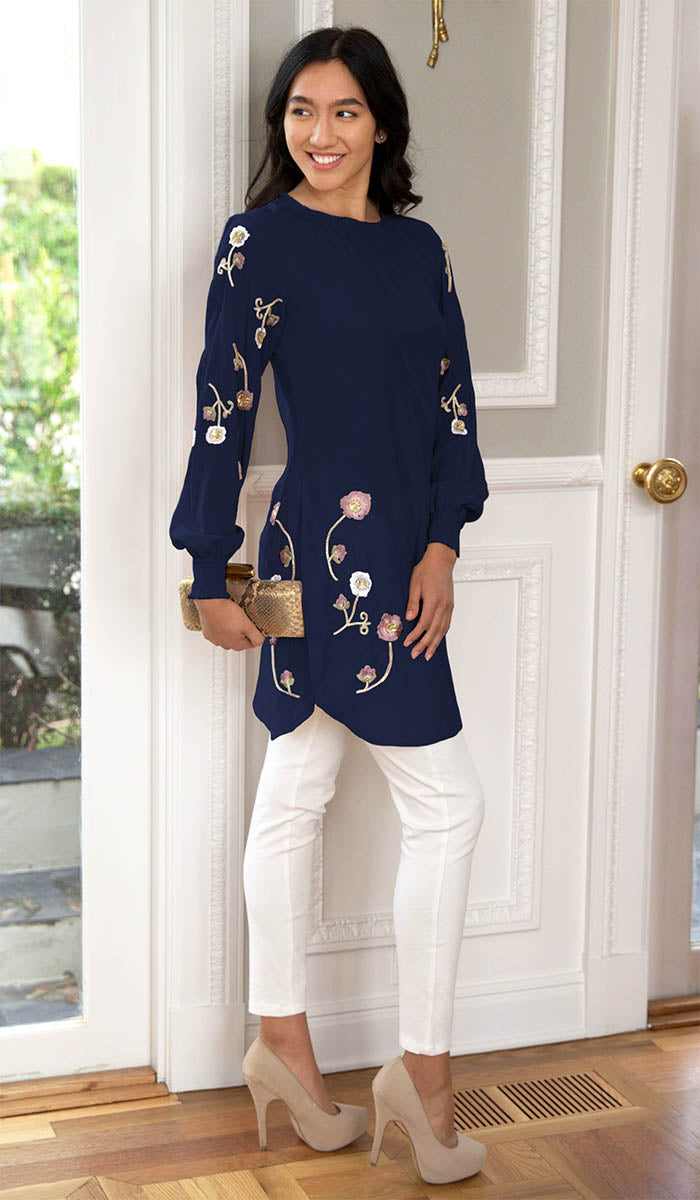 Model in front of a door wearing Iman embroidered tunic in Navy with white pants, heels, and a clutch. 