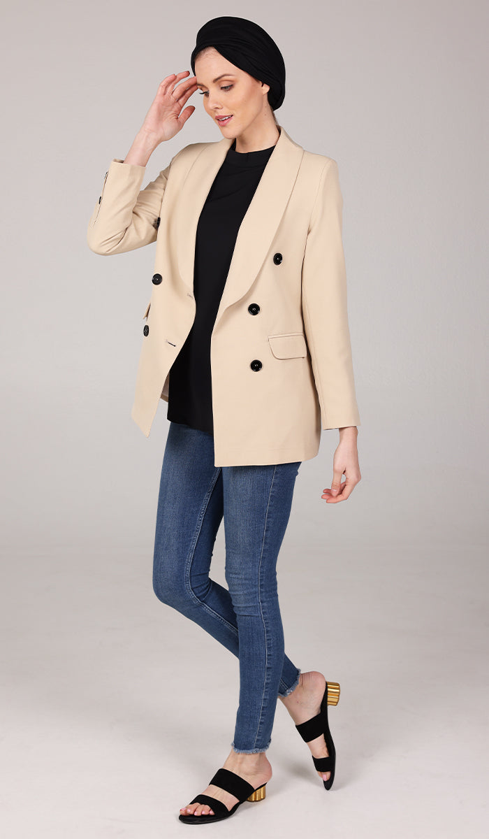 Side view of woman wearing black turban with a cream vanilla jacket blazer with blue jeans.