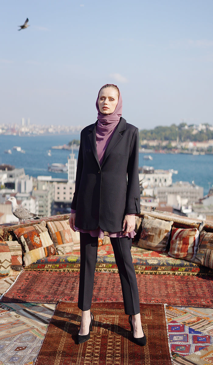 Full view of woman with dusty mauve hijab and top wearing a black blazer with black pants.