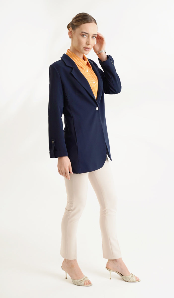 Full body view of woman wearing an orange top inside a navy blue blazer with cream pants.