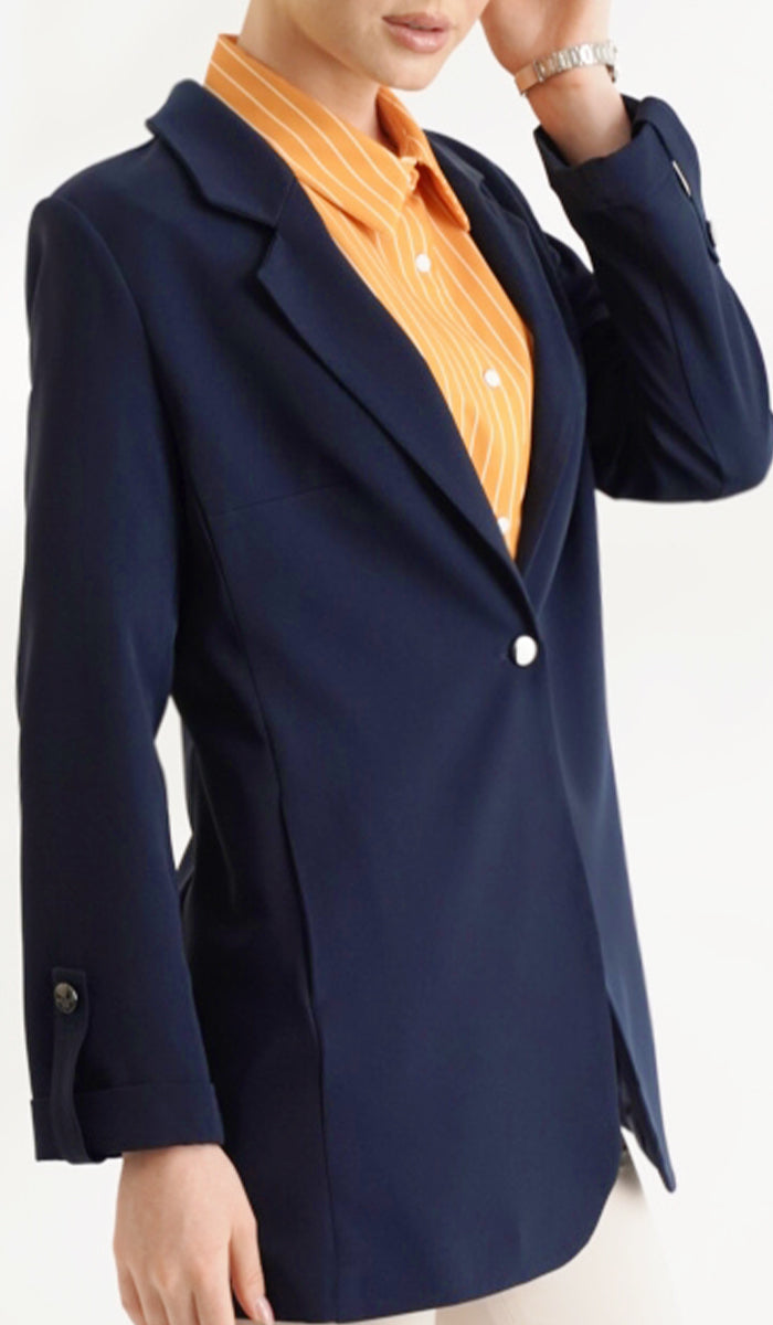 close up of woman wearing an orange top inside a navy blue blazer with cream pants.